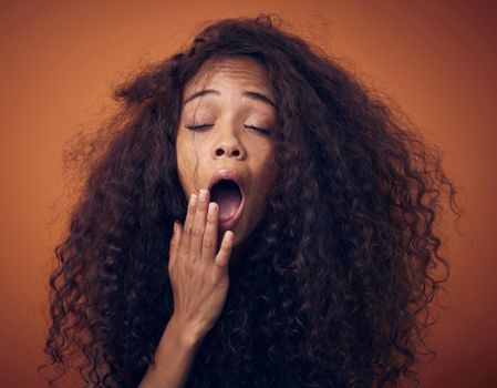 Im tired of haircare products thats not doing what theyre supposed to do. Shot of a young woman with curly hair yawning against an orange background.