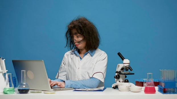 Portrait of crazy female chemist working on laptop at desk