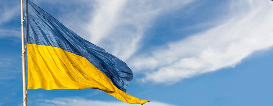 Large national flag of Ukraine flies in the blue sky. Big yellow blue Ukrainian state banner. Independence, flag, Constitution Day, National Holiday, text space.