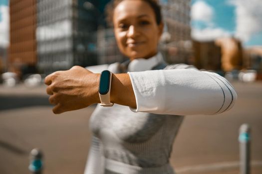 Sportswoman using fitness smart watch while jogging outdoors on a sunny day