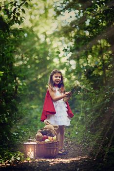 Exploring the wonder of the woods. Portrait of a little girl dressed in a red cape holding some flowers in the woods.