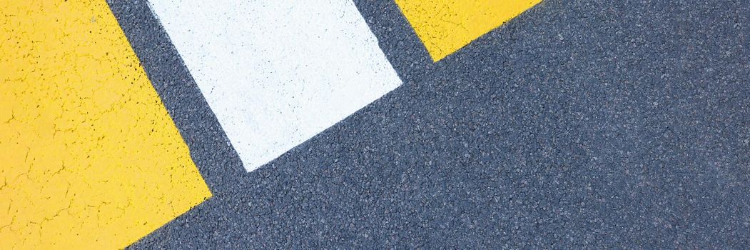 Closeup of yellow and white stripes on gray asphalt background