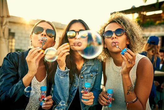 No moment spent blowing bubbles was ever wasted. Shot of a group of young women blowing bubbles together outdoors.