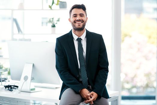 Id like to think the white collar life chose me. Cropped portrait of a handsome young businessman smiling while sitting on his desk in a modern office.
