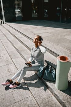 Woman in light gray sportswear sitting outdoors with eyes closed