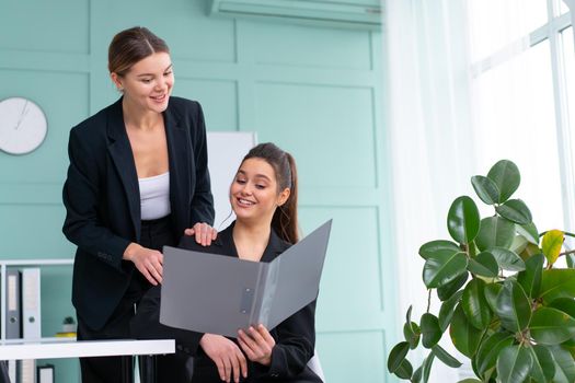 Young women leaders are checking financial statements from paper documents. Two female confident business worker dressed black suit in office checking financial document