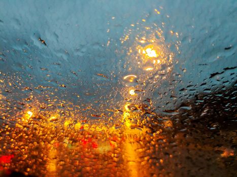 Raindrops on the windshield of the car. There is a lot of traffic, the lights of cars are reflected.