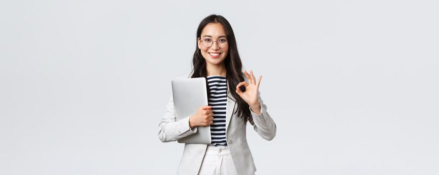 Business, finance and employment, female successful entrepreneurs concept. Young confident businesswoman in glasses, showing okay gesture, hold laptop, guarantee best service quality