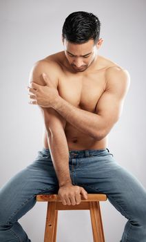 Deciding which pose works best. Studio shot of a handsome young man showing off his muscular body while sitting on a chair against a grey background.