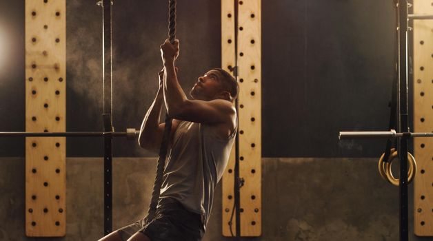 Climb your way to the top. Shot of a muscular young man climbing a rope in a gym.