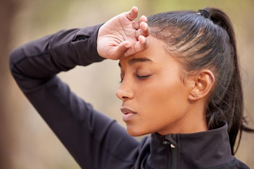 Headaches can ruin any plans. Shot of a young woman experiencing a headache while out jogging in the forest.
