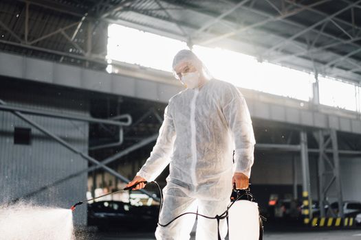 Man dressed white protective overalls spraying surface antibacterial sanitizer sprayer during quarantine