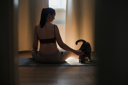 young woman doing yoga and practising meditation with her cat at home. mental health concept