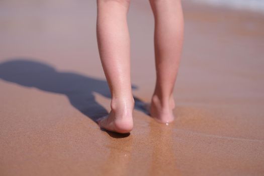 Wet bare feet walk along beach along sea closeup