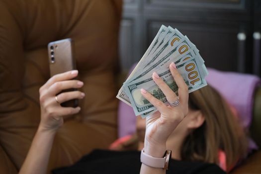 Woman holds smartphone and holds it with dollars