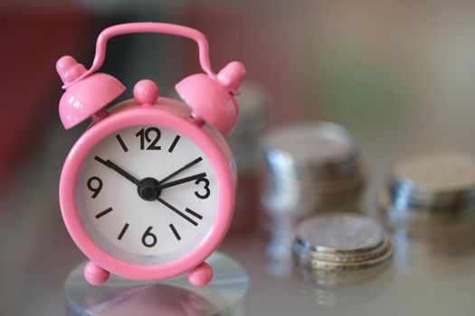 Pink alarm clock compass and stacks of coins closeup