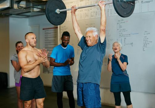 Impossible is nothing. Shot of a senior man lifting weights while a group of people in the background watch on.