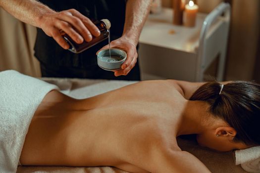 Masseur man therapist pouring warm herb infused oil to make back massage