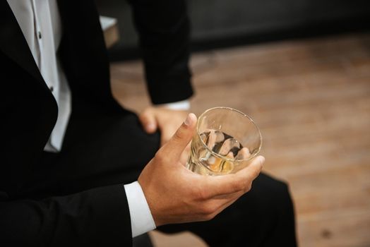 a glass of whiskey in the hand of a man in a black suit
