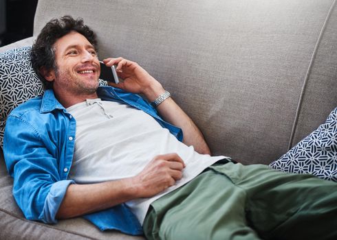 Just chilling, and you. Shot of a happy bachelor answering his cellphone while relaxing on the couch at home.