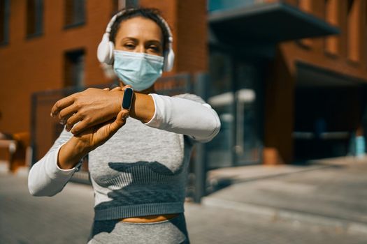 Woman in protective mask and headphones adjusting her smart watch