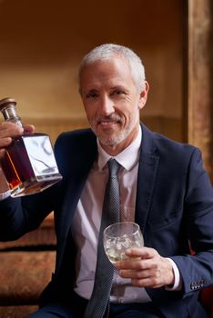 Theres nothing better than a fine whiskey. Portrait of a well-dressed mature man holding a glass and whiskey bottle in a bar after work.