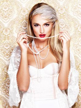 The good old days of glamour. A beautiful and glamourous blonde woman in a vintage outfit holding up a string of pearls with an alluring gaze.
