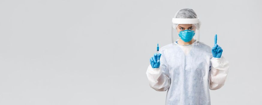 Covid-19, medical research, diagnosis, healthcare workers and quarantine concept. Determined doctor in PPE costume, personal protective equipment, hold syringe with coronavirus vaccine for patient