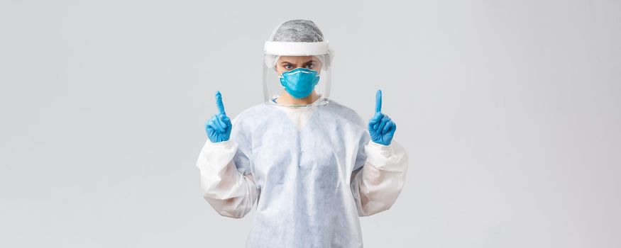 Covid-19, preventing virus, health, healthcare workers and quarantine concept. Angry confident doctor or nurse in respirator, PPE medical suit and gloves, frowning and pointing fingers up