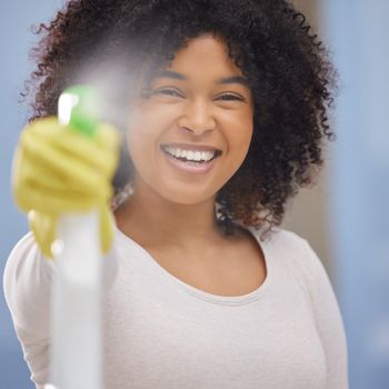 Goodbye fingerprints. Shot of an attractive young woman standing alone and spraying a bottle of detergent while doing the chores at home.