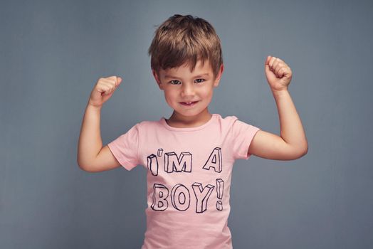 Tough guys wear pink. Studio portrait of a cheering boy wearing a shirt with Im a boy printed on it against a gray background.