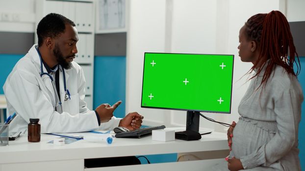 African american people looking at greenscreen on computer in cabinet. Pregnant woman and medic using blank copyspace template with isolated mockup chroma key background. Tripod shot.