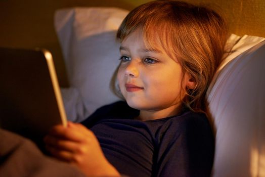 Reading my bedtime story online. A little girl lying in bed with a digital tablet.