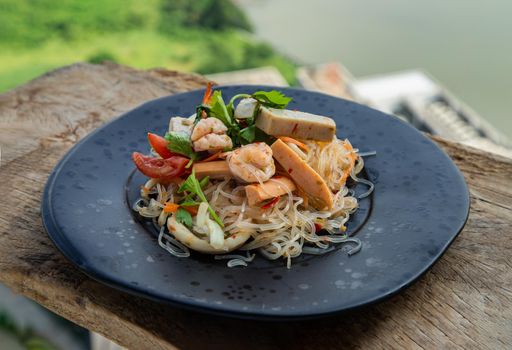 Seafood spicy glass noodle salad or Spicy delicious Mung bean Noodle Salad with fresh seafood (Yum woon sen) on wooden table. 
