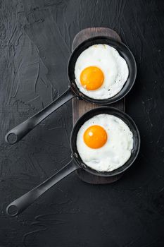 Fried eggs with cherry tomatoe and bread for breakfast in cast iron frying pan, on black background, top view flat lay