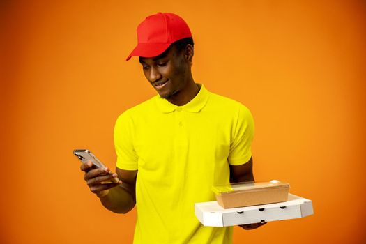 African delivery man wearing courier uniform holding cardboard parcel using smartphone