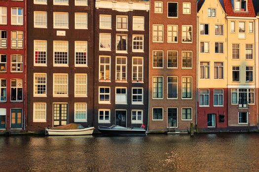 Hhouses and boats on Amsterdam canal pier Damrak on sunset