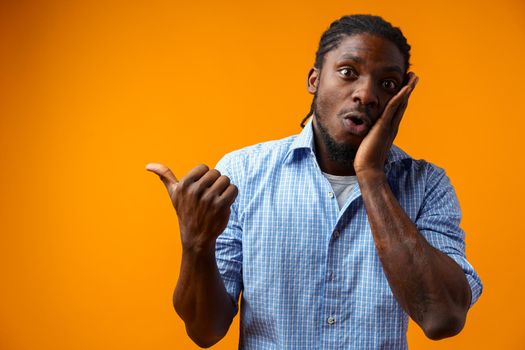 Young african american man pointing at copy space over yellow background