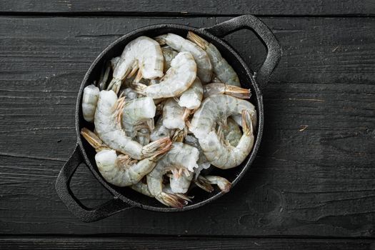 Healthy organic tiger shrimps, in cast iron frying pan, on black wooden background, top view flat lay