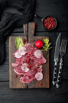 Classic beef carpaccio, with Radish and garnet, on wooden serving board, on black wooden table background, top view flat lay