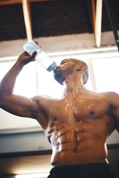 He went full on beast mode. Low angle shot of a muscular young man drinking water while exercising in a gym.