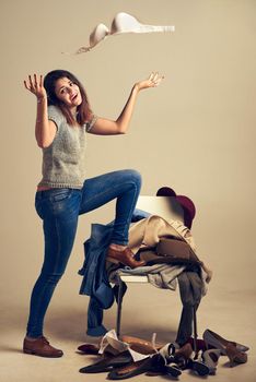 Thats it Ill just stick with jeans and a shirt. Studio shot of a young woman choosing clothing piled on a chair against a brown background.