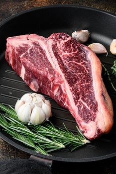 Raw T-bone Steak for grill or BBQ with ingredients, on frying cast iron pan, on old dark rustic background