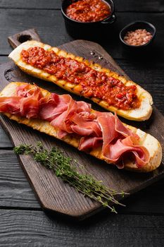 Italian tomato, prosciutto, jamon, ham and cheese bruschetta, on black wooden table background
