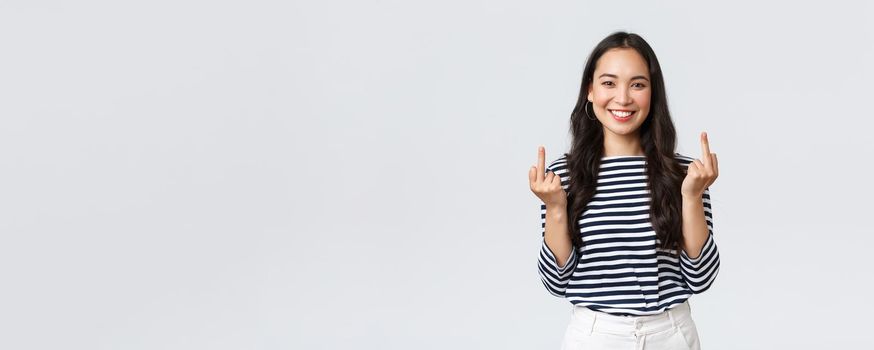 Lifestyle, beauty and fashion, people emotions concept. Unbothered and careless young happy smiling woman dont give a damn, showing middle fingers and feeling good, white background