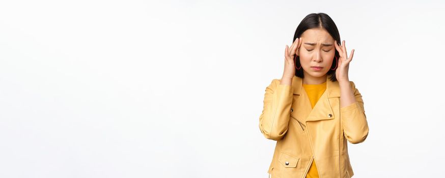 Image of asian woman massaging head temples with concerned face, suffering headache, migraine, standing over white background