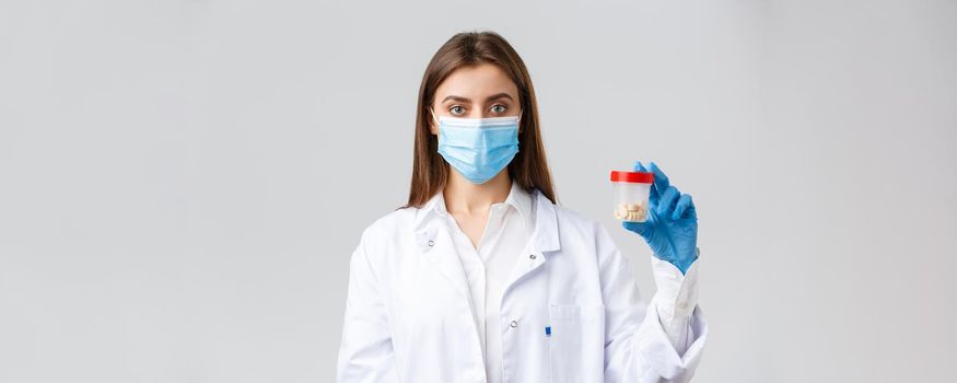 Covid-19, preventing virus, healthcare workers and quarantine concept. Doctor in scrubs and medical mask, showing container with pills, recommend vitamins or antibiotics