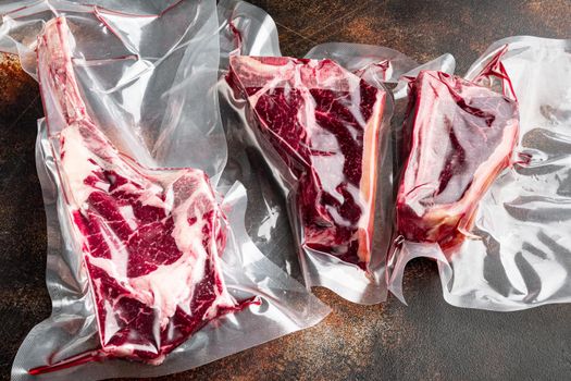 Raw beef dry aged steak vacuum sealed bag for sell, tomahawk, t bone and club steak cuts, on old dark rustic background