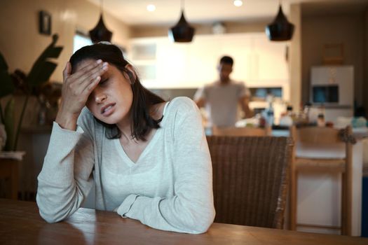 I need to get out. Shot of a woman looking stressed while sitting at home with her boyfriend standing in the background.