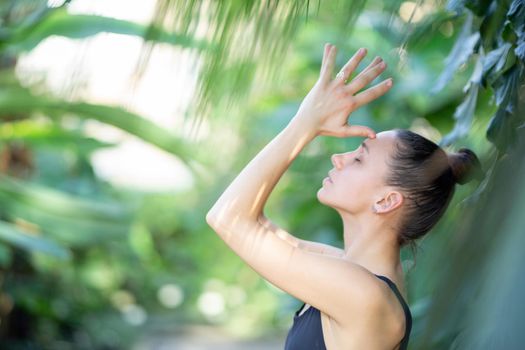 Female meditating and practicing yoga in tropical rainforest. Beautiful young woman practicing yoga outdoor with tropical forest in background